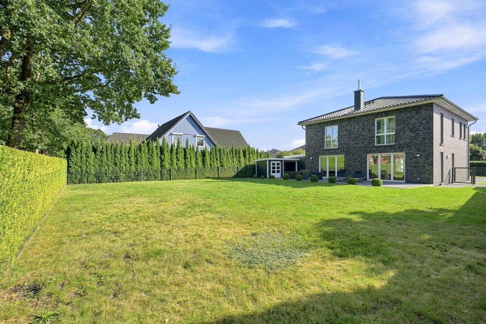 Garten des Stadthauses in Bad Bramstedt mit Rasenfläche, Hecke und Geräteschuppen.